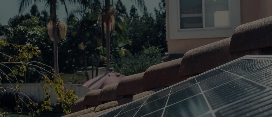 Close-up of solar panels on a tiled roof with trees and a building in the background.