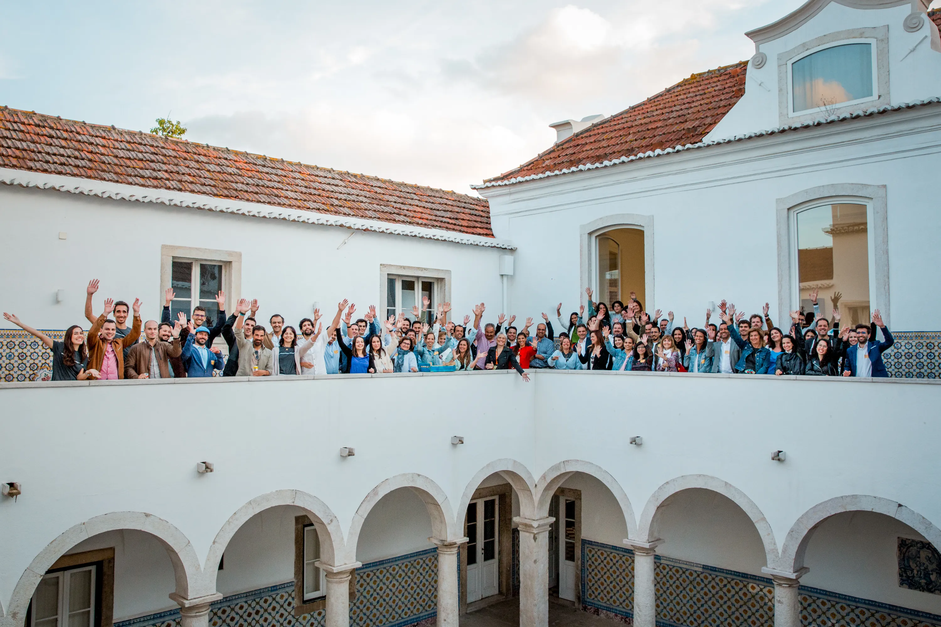 Large group of people standing on a balcony with arms raised, smiling at the camera.