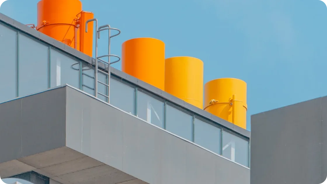 Modern building rooftop with bright orange cylindrical ventilation ducts against a clear blue sky.