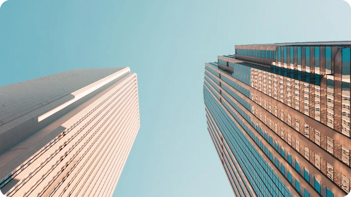 Upward view of two tall skyscrapers against a clear blue sky.