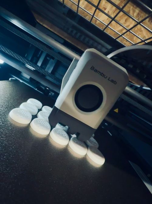 Close-up of a Bambu Lab 3D printer nozzle printing multiple white circular objects on the print bed.