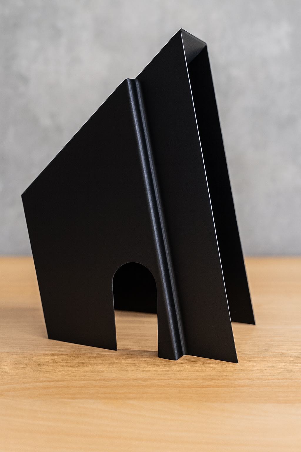 Black metal bookend with an arched cutout on a wooden surface.