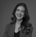 Black and white portrait of a smiling woman with long wavy hair wearing a blazer and earrings.