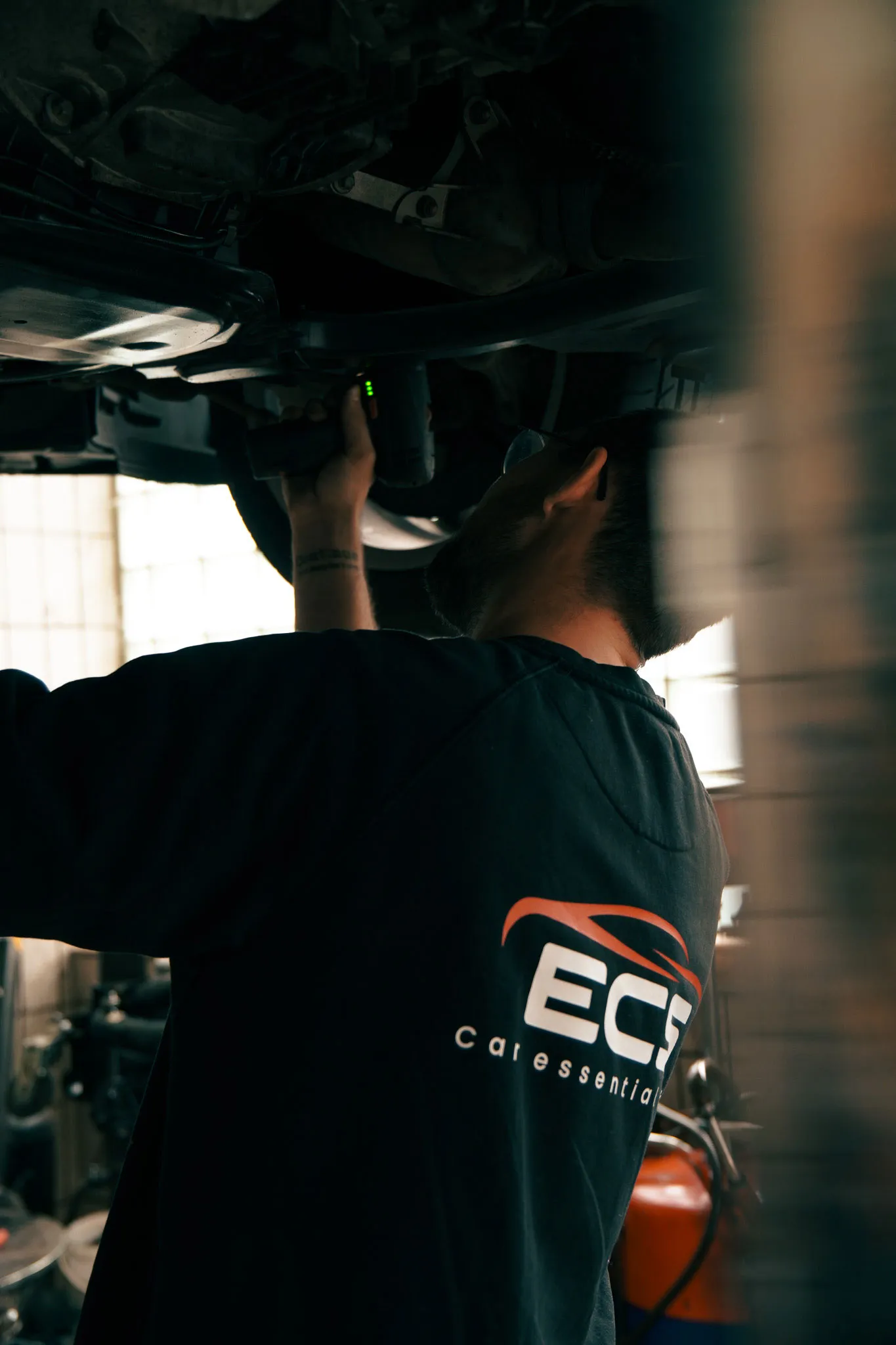 Ein Mechaniker inspiziert die Unterseite eines Fahrzeugs mit einer Taschenlampe in einer Werkstatt.