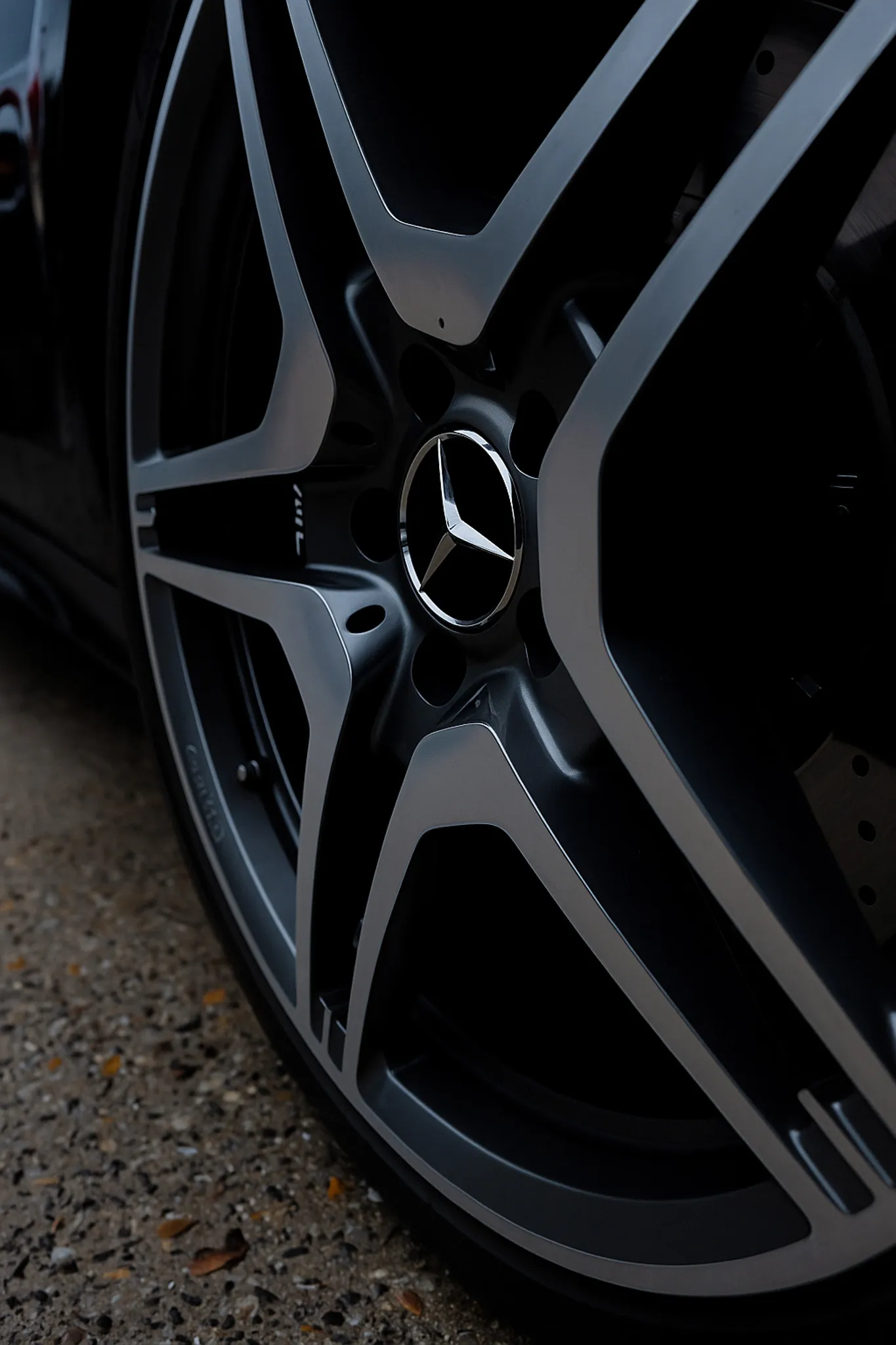 Nahaufnahme eines schwarzen Mercedes-AMG-Felgenrads mit silbernen Akzenten auf einem gepflasterten Boden.