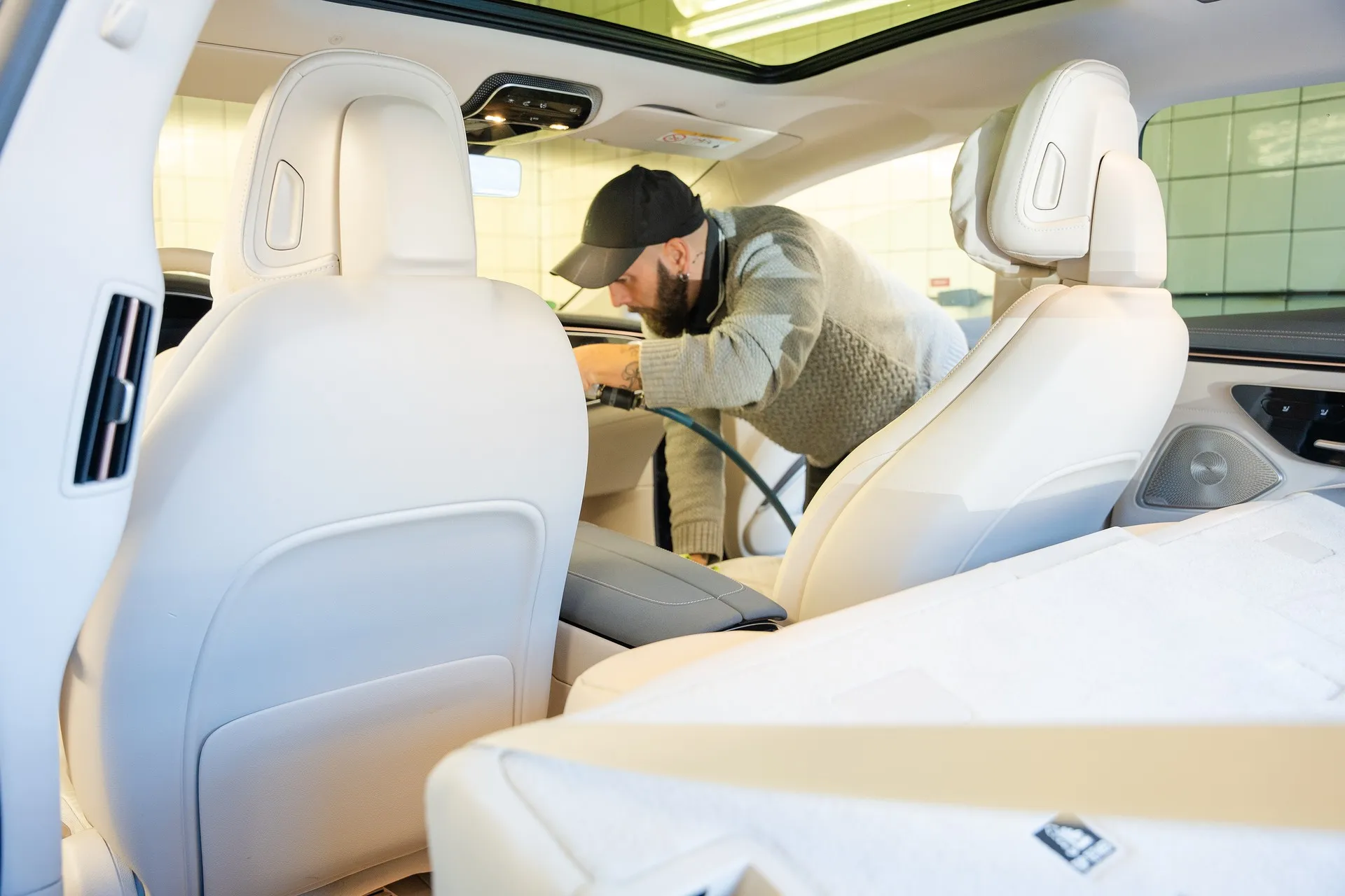 Mann reinigt den Innenraum eines Fahrzeugs mit einem Staubsauger, gesehen von hinten durch die vorderen Sitze.