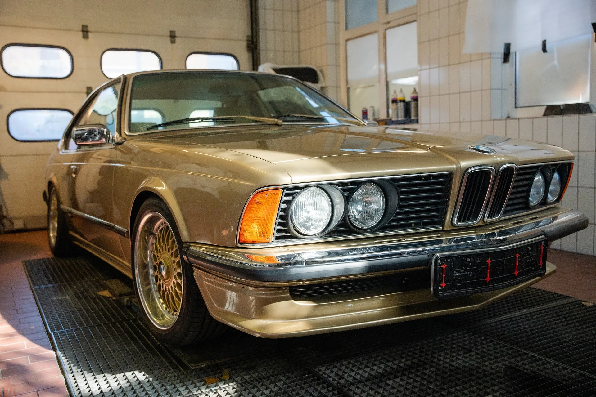 Goldfarbener BMW Oldtimer in einer Autowerkstatt mit Fokus auf Front und Scheinwerfer.