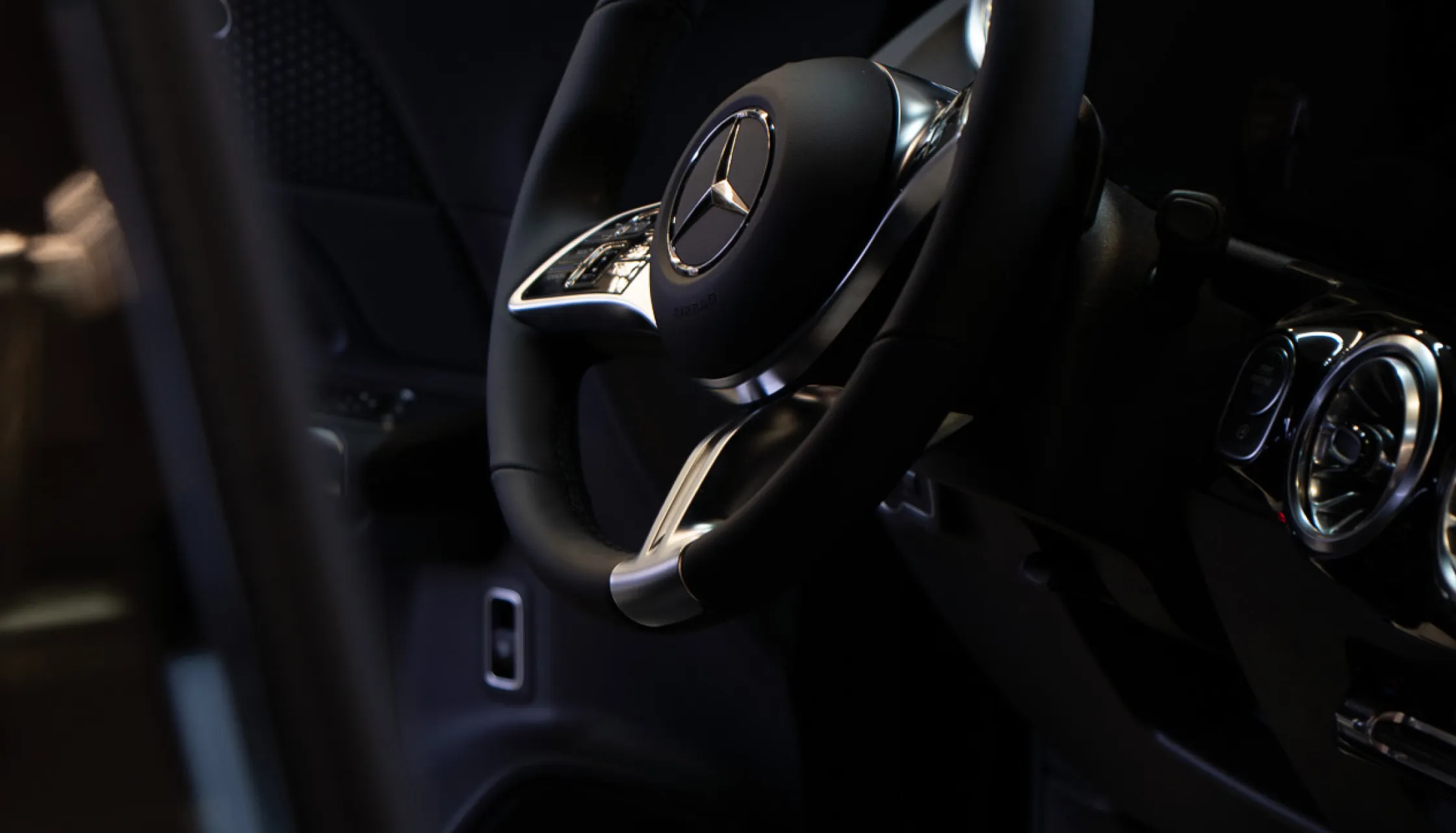 Nahaufnahme des Lenkrads eines Mercedes-Benz mit schwarzem Leder und silbernen Akzenten im Fahrzeuginneren.