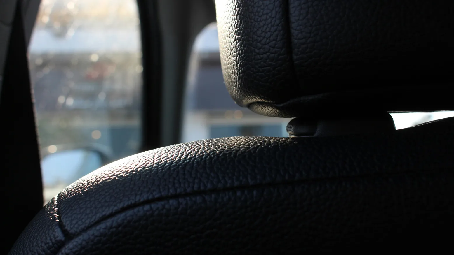 Nahaufnahme eines schwarzen Lederkopfteils und einer Kopfstütze in einem Auto mit unscharfem Hintergrund durch das Fenster.