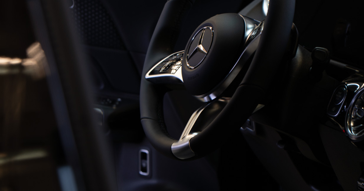 Nahaufnahme eines schwarzen Mercedes-Ledersportlenkrads mit silbernen Akzenten im Innenraum des Autos.