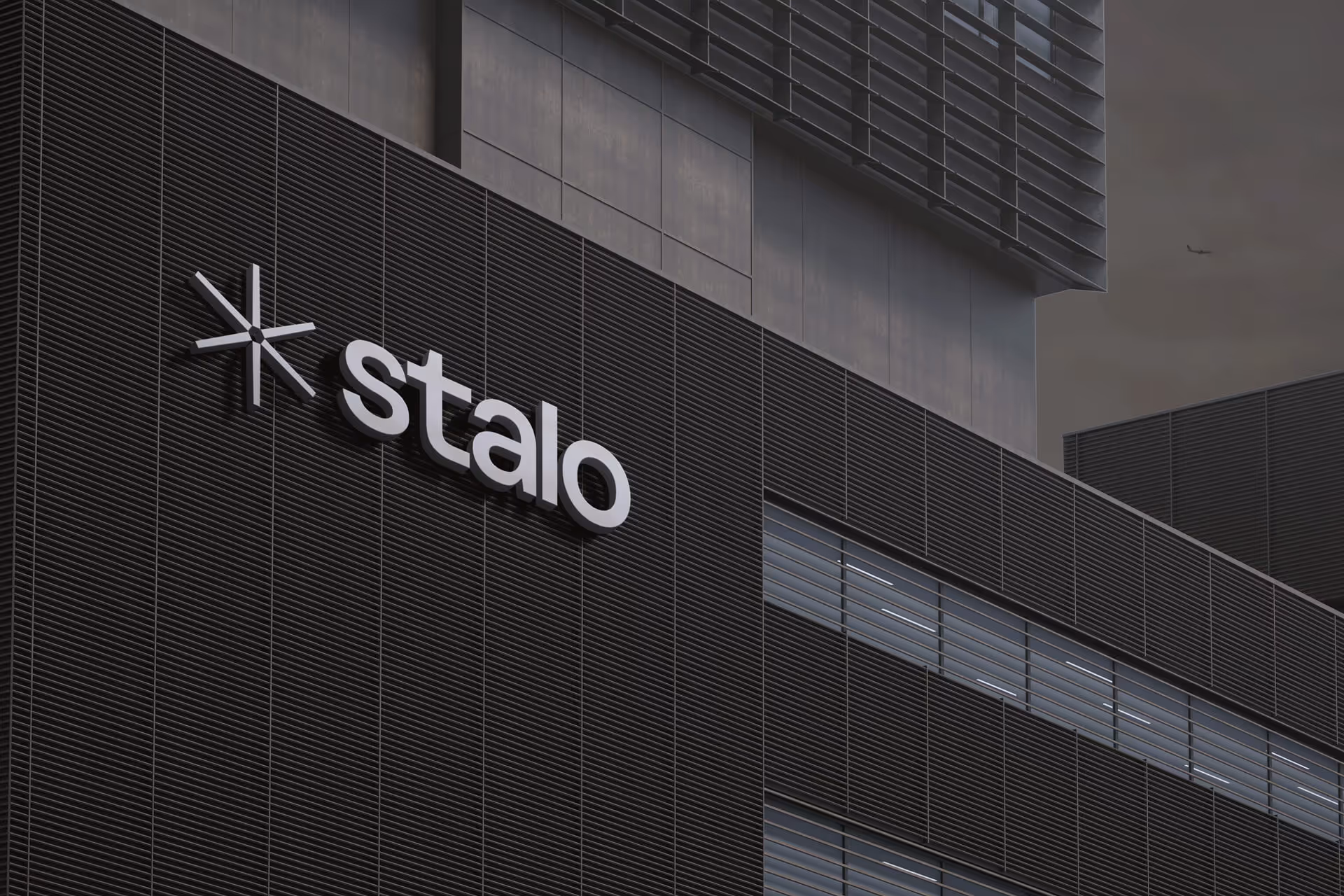 Fachada de prédio comercial escuro com o logotipo "stalo" iluminado em branco.