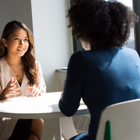 Duas mulheres conversando animadamente sentadas à mesa em um ambiente bem iluminado.