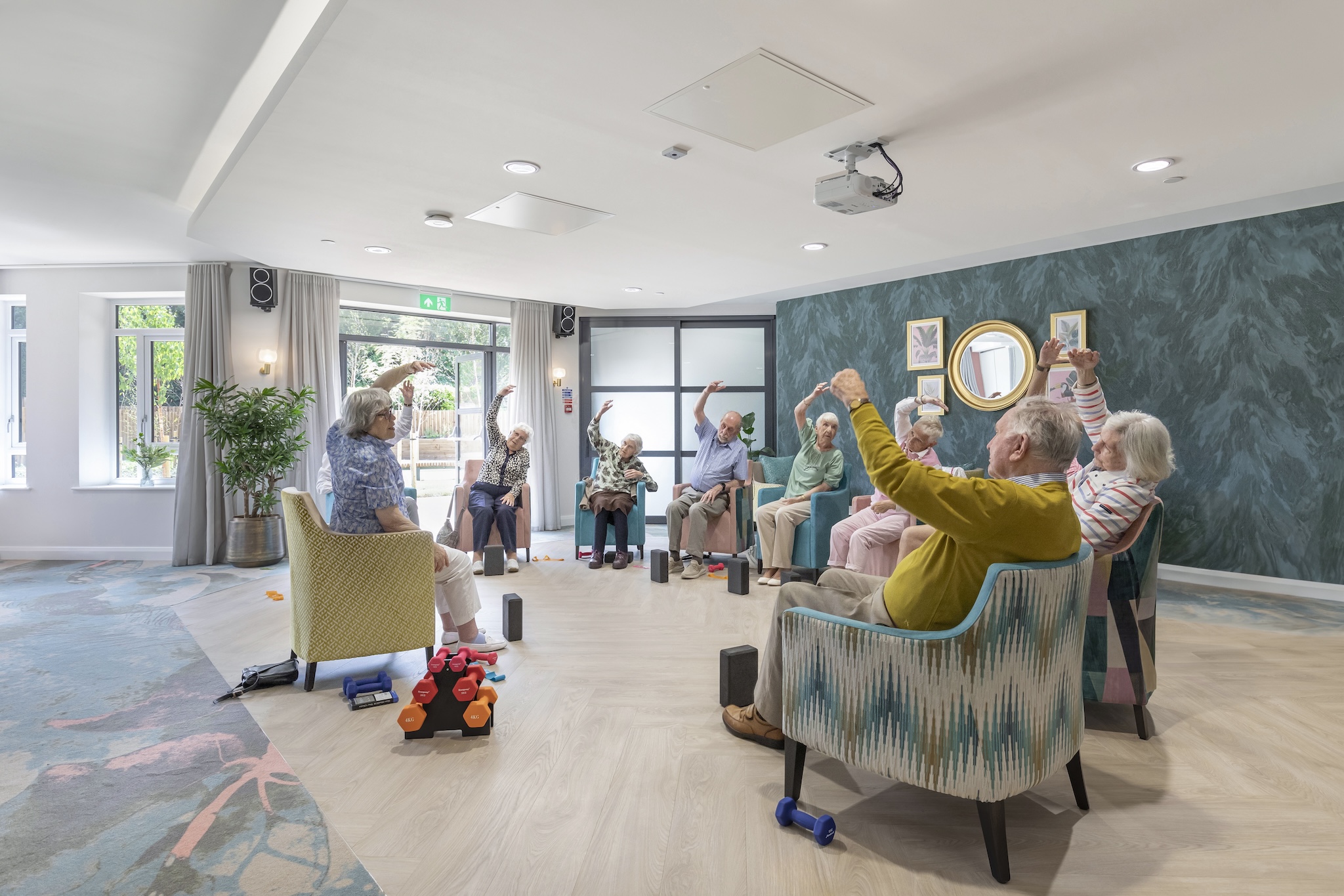 Neighbours at Birchgrove Retirement Apartments take part in a seated movement class in a shared lounge.