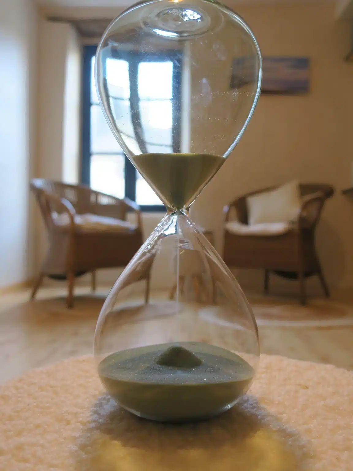 Sablier posé au premier plan dans le cabinet d’hypnose d’Erika Jambou à Landerneau, avec les fauteuils en rotin en arrière-plan.