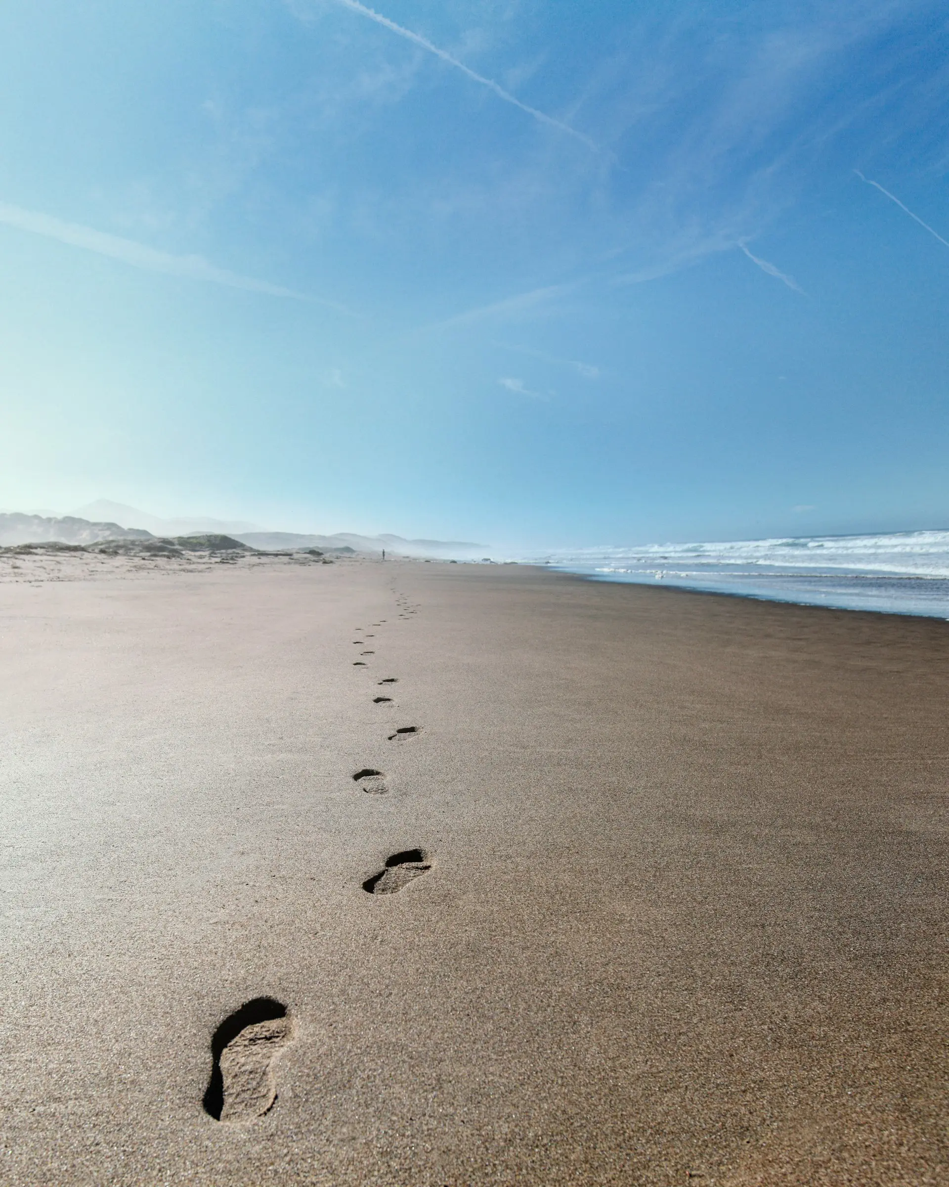 Empreintes de pas sur une longue plage au bord de l’océan, symbolisant le cheminement personnel et l’apaisement.