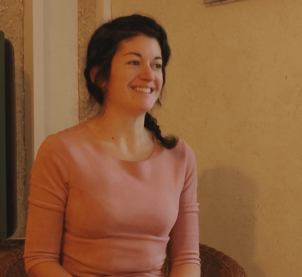 Erika Jamou souriante assise dans un fauteuil en rotin, dans une pièce chaleureuse aux tons naturels.