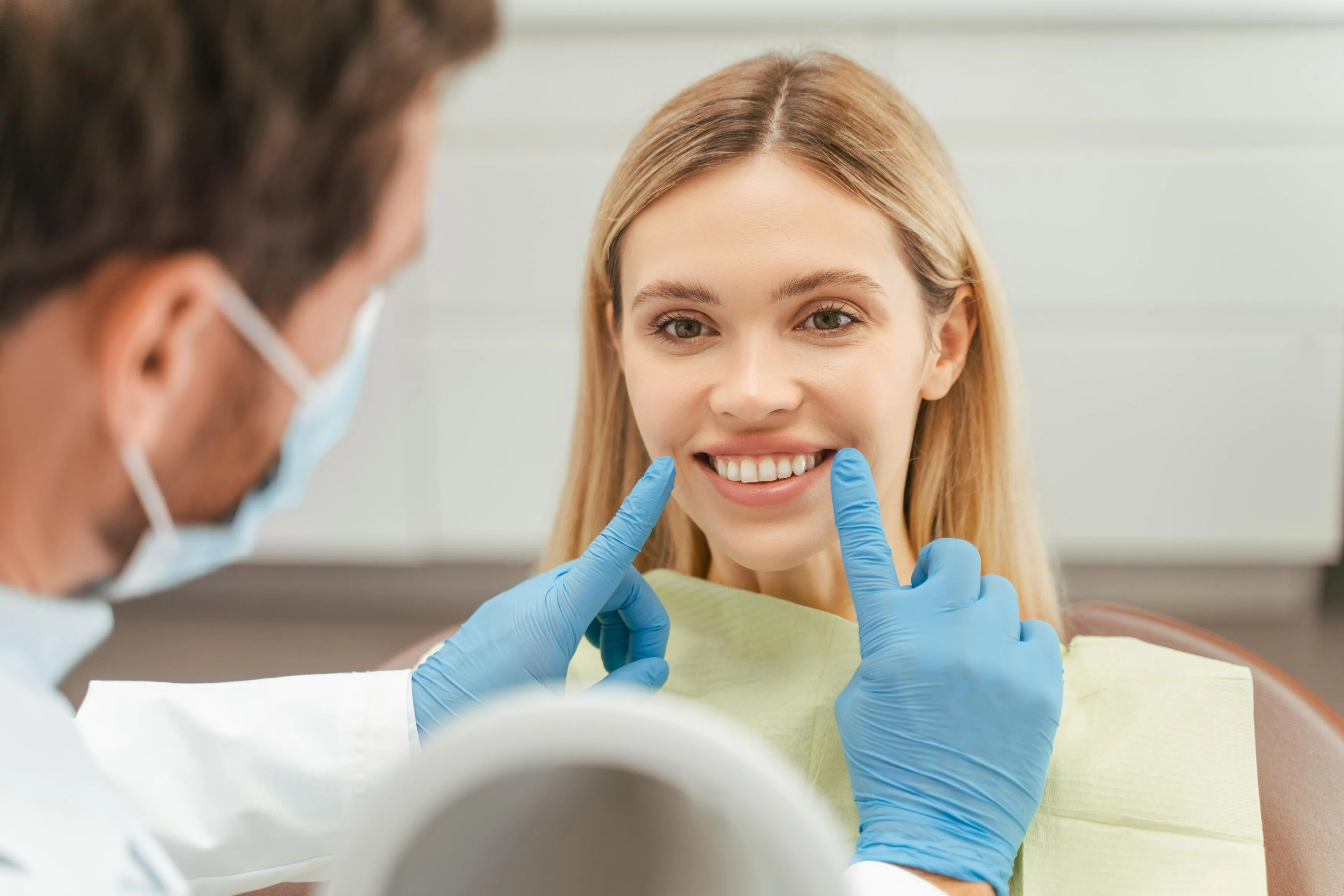 A dentist holds a tooth shade guide next to a patient’s smile to select the ideal color for cosmetic dental treatments such as veneers or whitening.