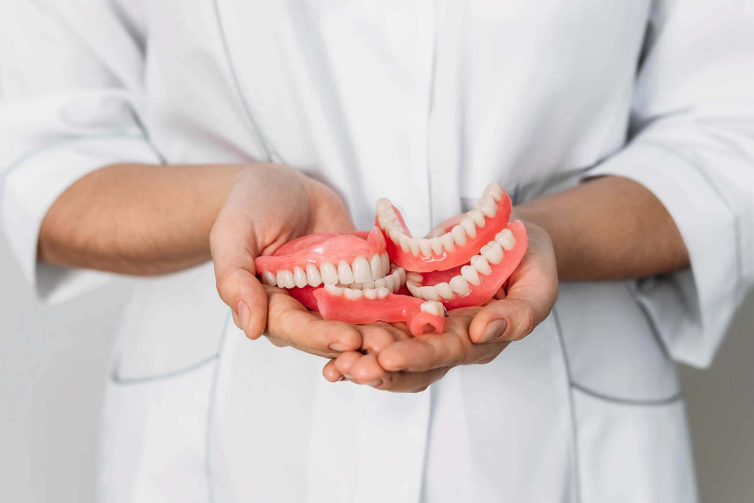 A dental professional holding a pair of full upper and lower dentures in both hands, showing the pink acrylic gums and natural-looking prosthetic teeth used to restore a complete smile.