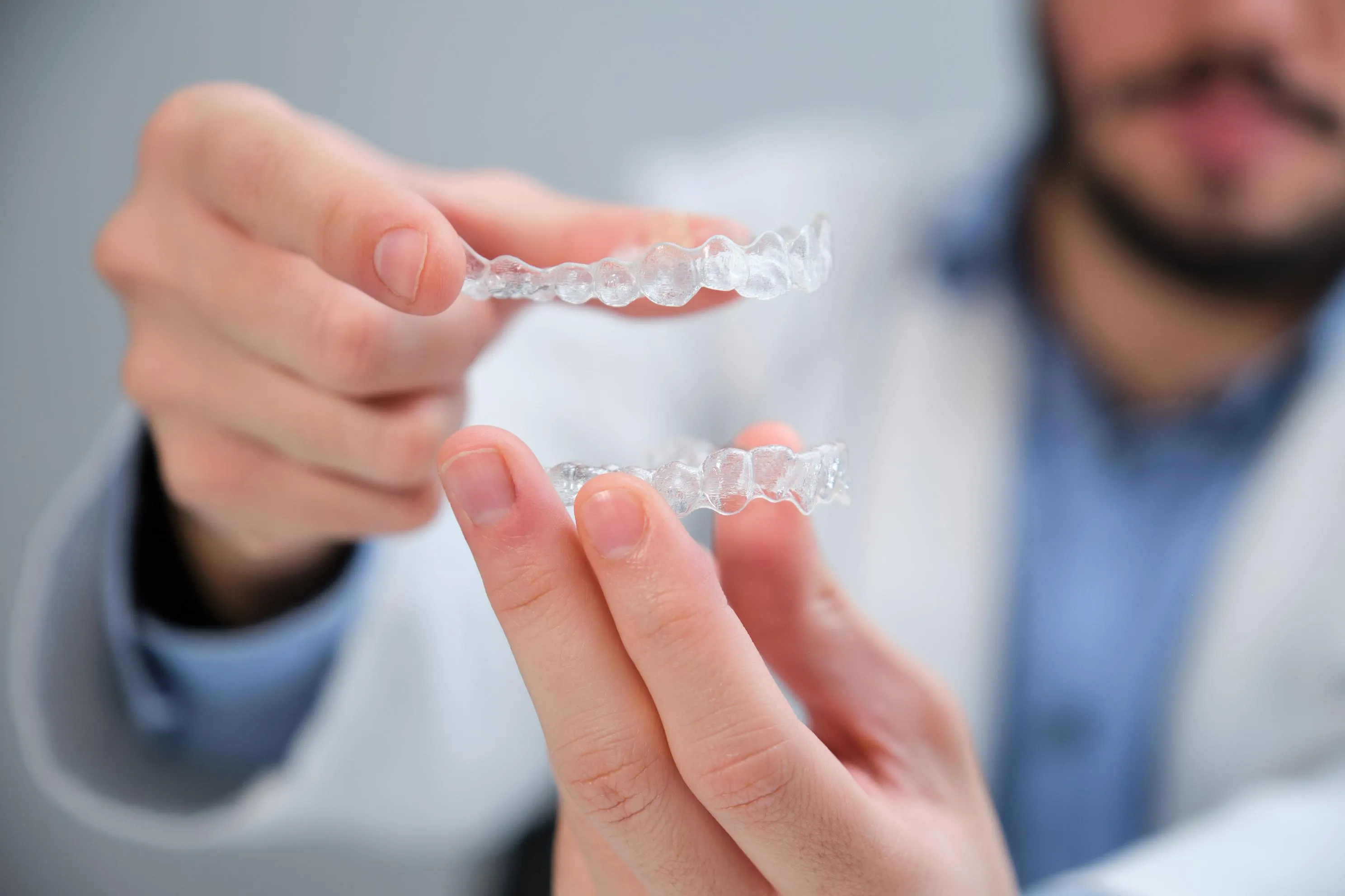 A dentist holds a clear aligner tray between both hands, showing the contoured shape and tooth-specific design used in clear aligner orthodontic treatment to gradually straighten teeth.