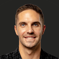 Tight headshot of a smiling man against a dark background, cropped just below the shoulders.