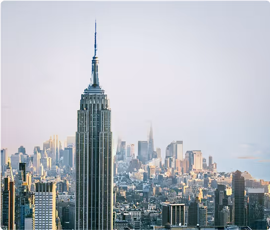 Empire State Building prominently in the foreground with New York City skyline and skyscrapers in the background under a clear sky.