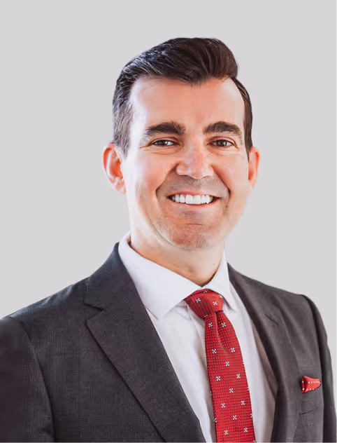 Smiling man in a dark suit, white shirt, and red patterned tie against a light gray background.