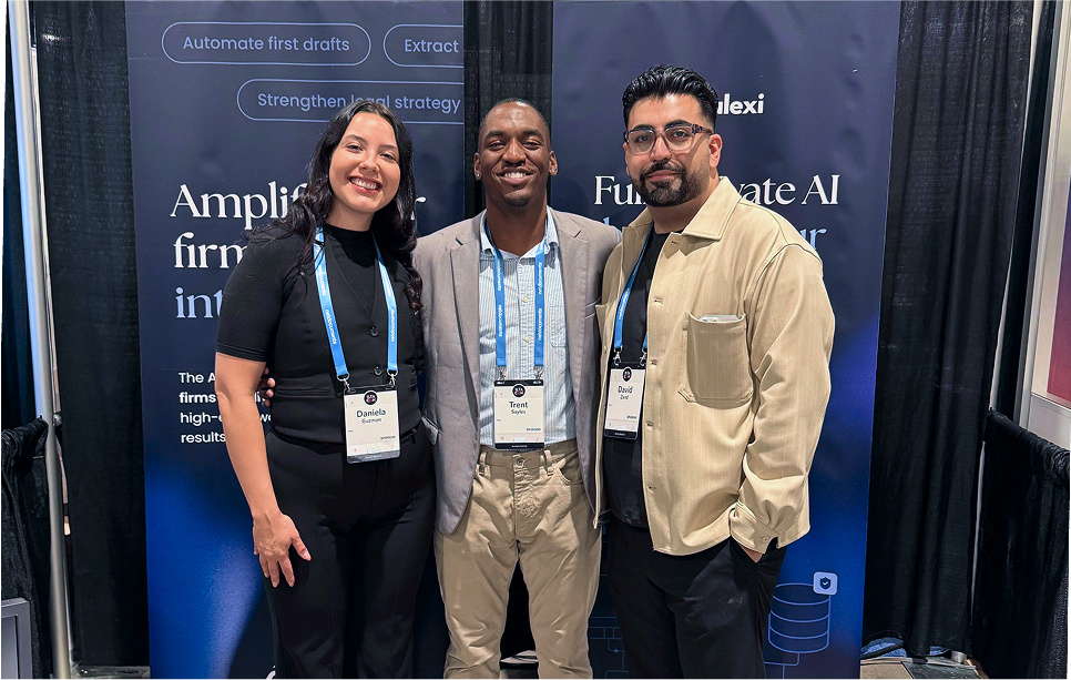 Three people smiling and posing together at a conference booth with blue AI-themed banners in the background.