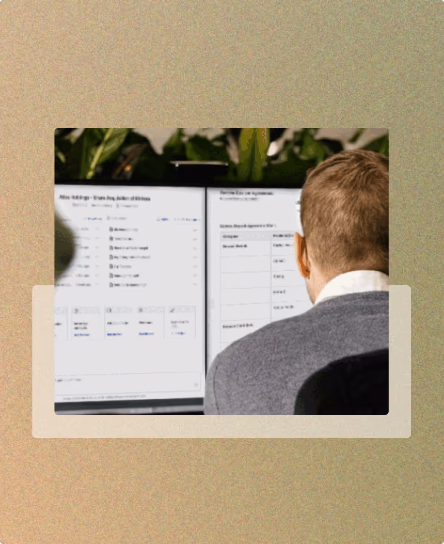 Rear view of a person with short hair and glasses looking at two computer screens displaying data and tables.