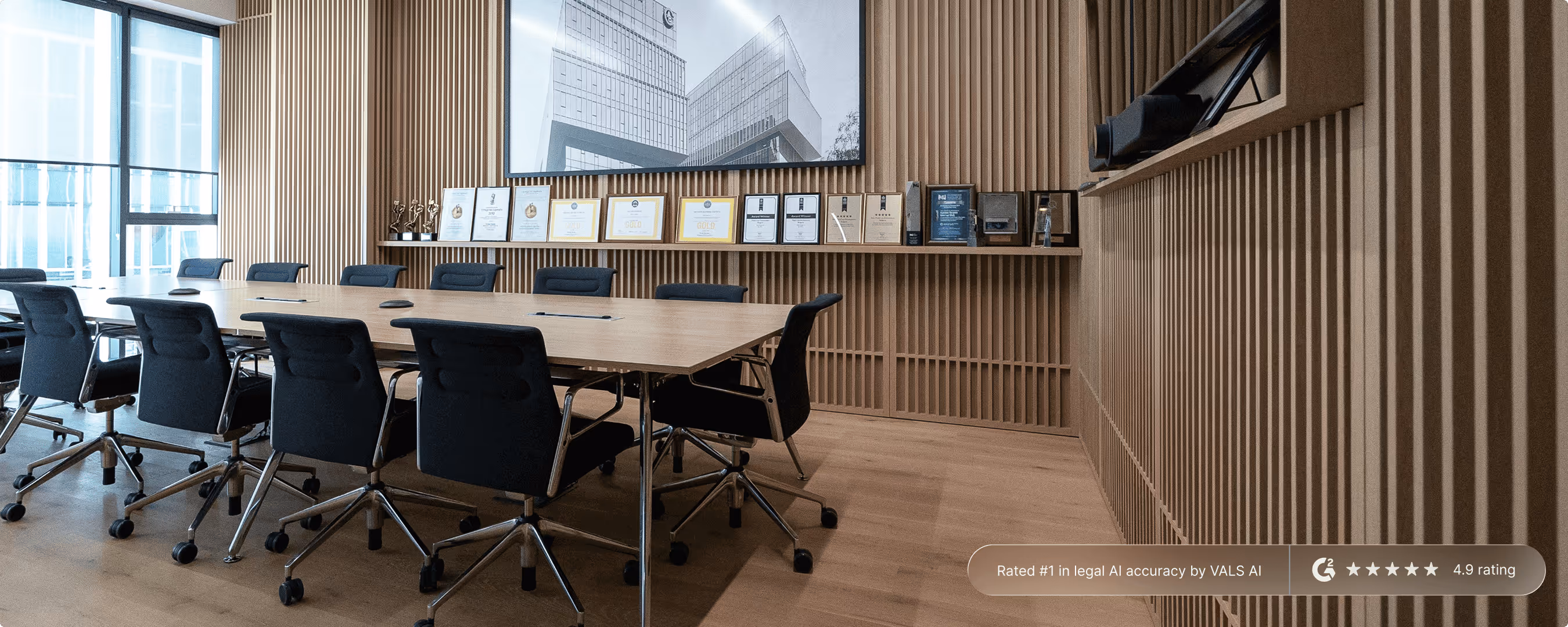 Modern conference room with wooden table, black office chairs, awards displayed on a shelf, and a large black-and-white architectural photograph on the wall.