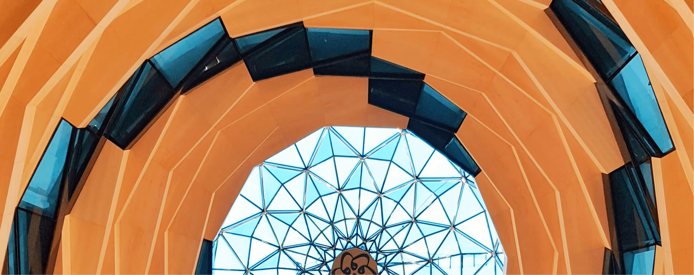Geometric modern architectural ceiling with orange layered panels and a central glass dome with triangular patterns.