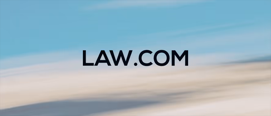 Black text displaying 'LAW.COM' centered on a blurred background with blue and beige tones.