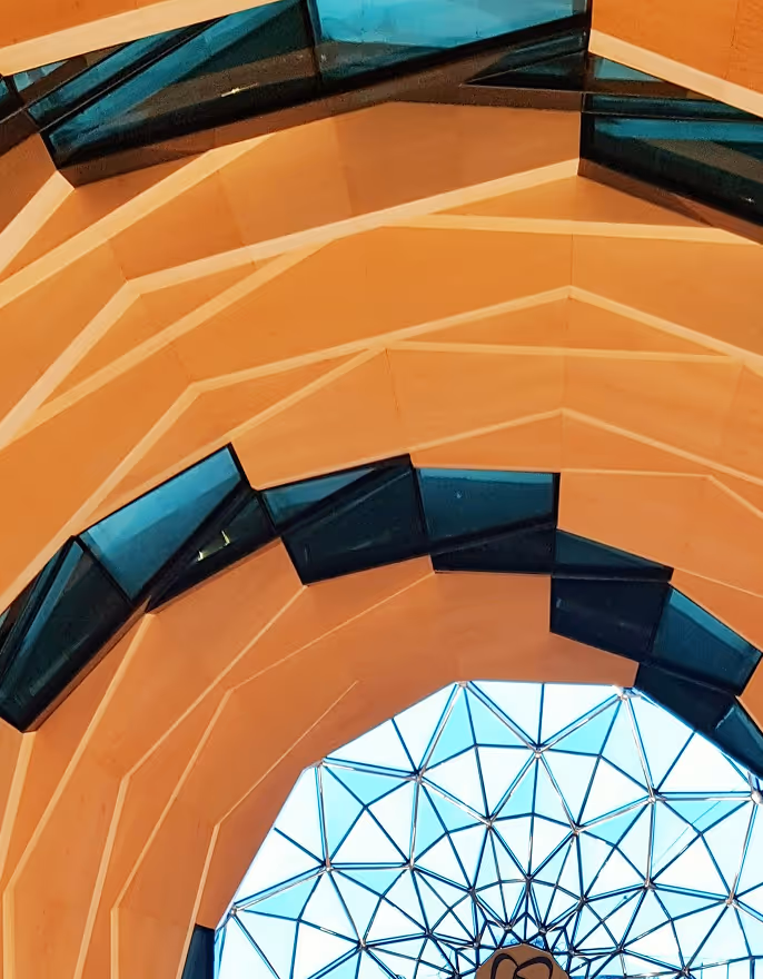 Interior view of a geometric dome ceiling with orange structural beams and blue glass panels.