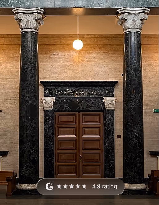Wooden double doors framed by black marble columns with ornate white capitals inside a building, under a round hanging light.