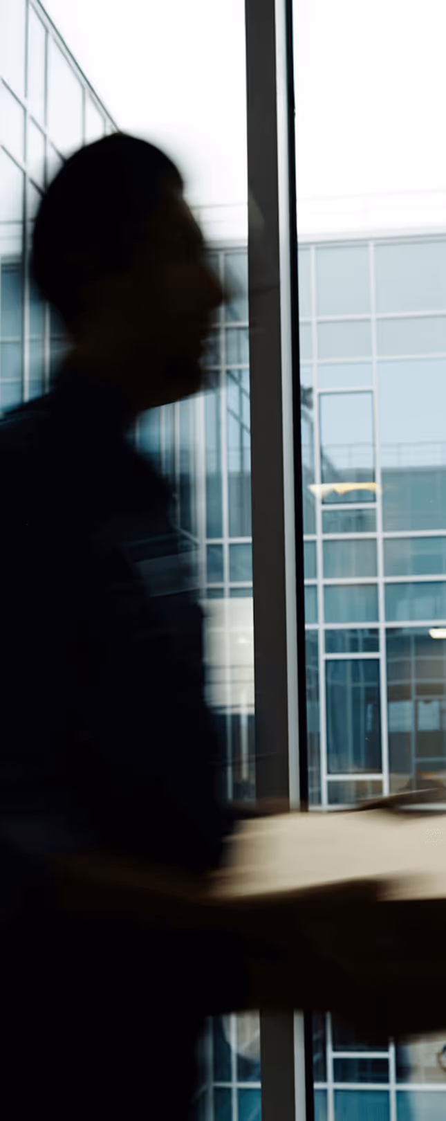Silhouette of a person carrying a box near large office building windows.