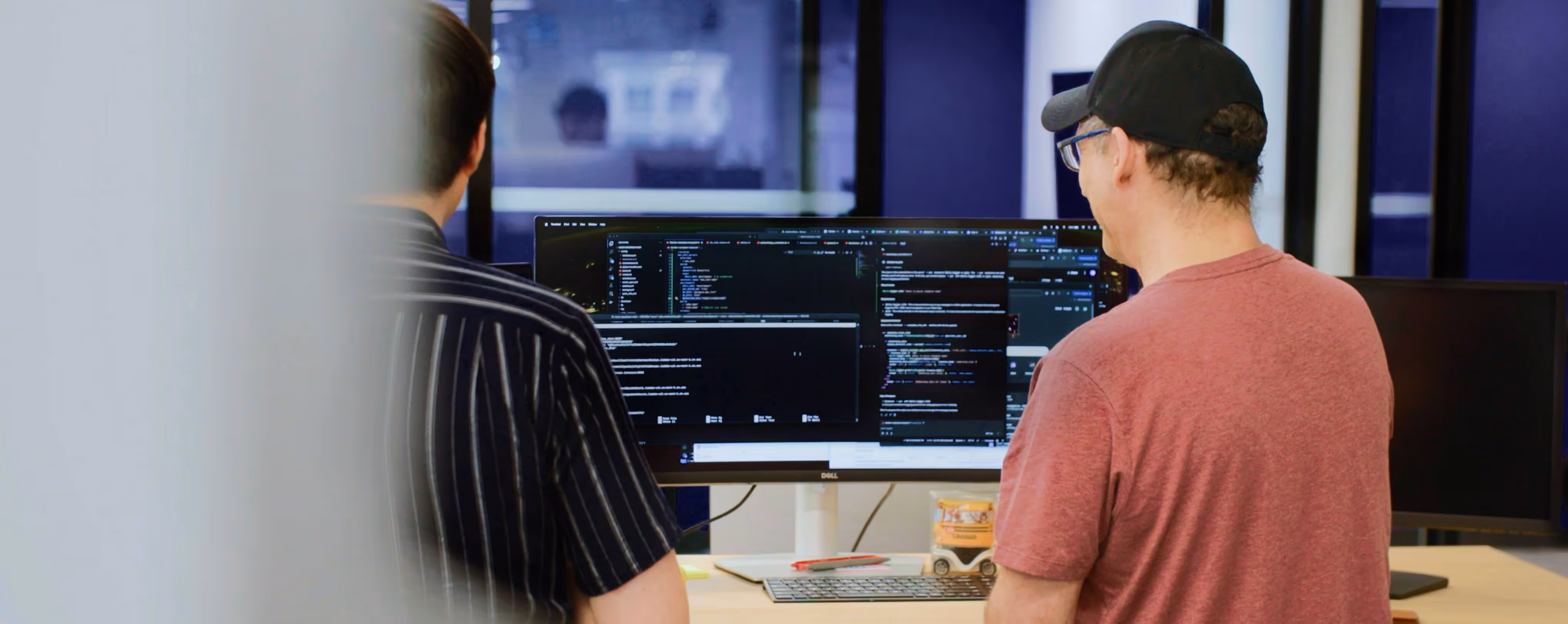 Two people standing and looking at a computer monitor displaying code in an office setting.
