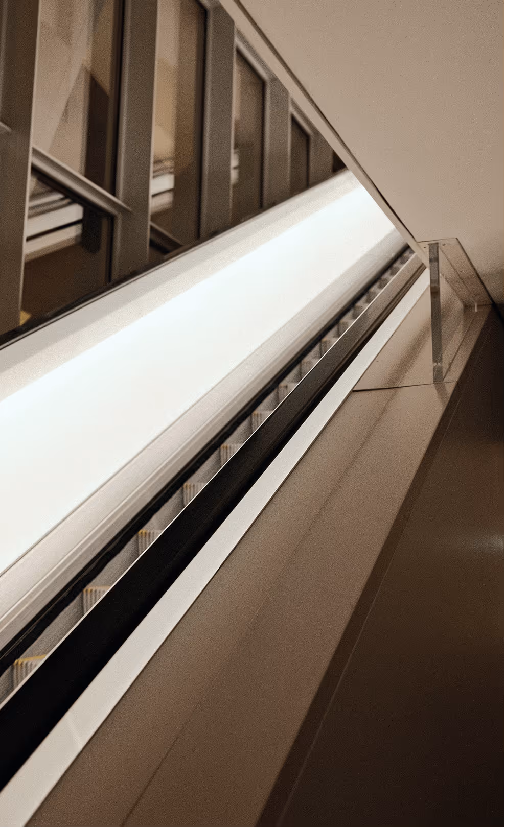Modern escalator viewed at an angle inside a building with reflective glass panels and sleek handrails.