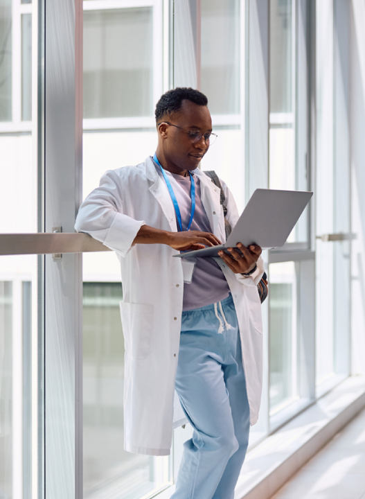 Doctor standing by a window with a laptop.