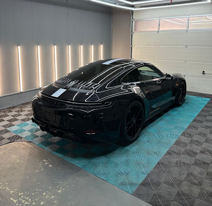 Sleek black sports car with tinted windows parked inside a modern garage with patterned flooring and vertical wall lights.