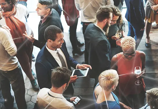 Eine diverse Gruppe von professionellen Unternehmern, die bei einem Networking Event socializen. Sie halten Getränke und Tablets, Handy in der Hand.