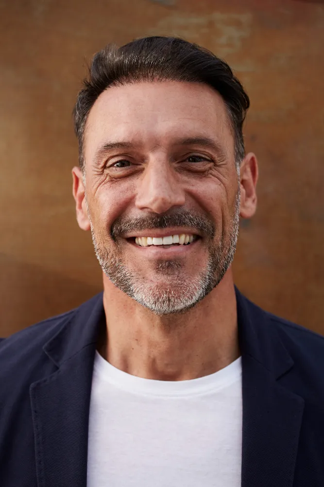 Smiling middle-aged man with short dark hair and a salt-and-pepper beard wearing a navy blazer and white shirt.
