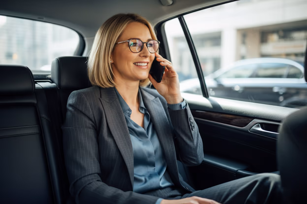 Femme d'affaires souriante en costume gris utilisant un téléphone dans la banquette arrière d'une voiture.
