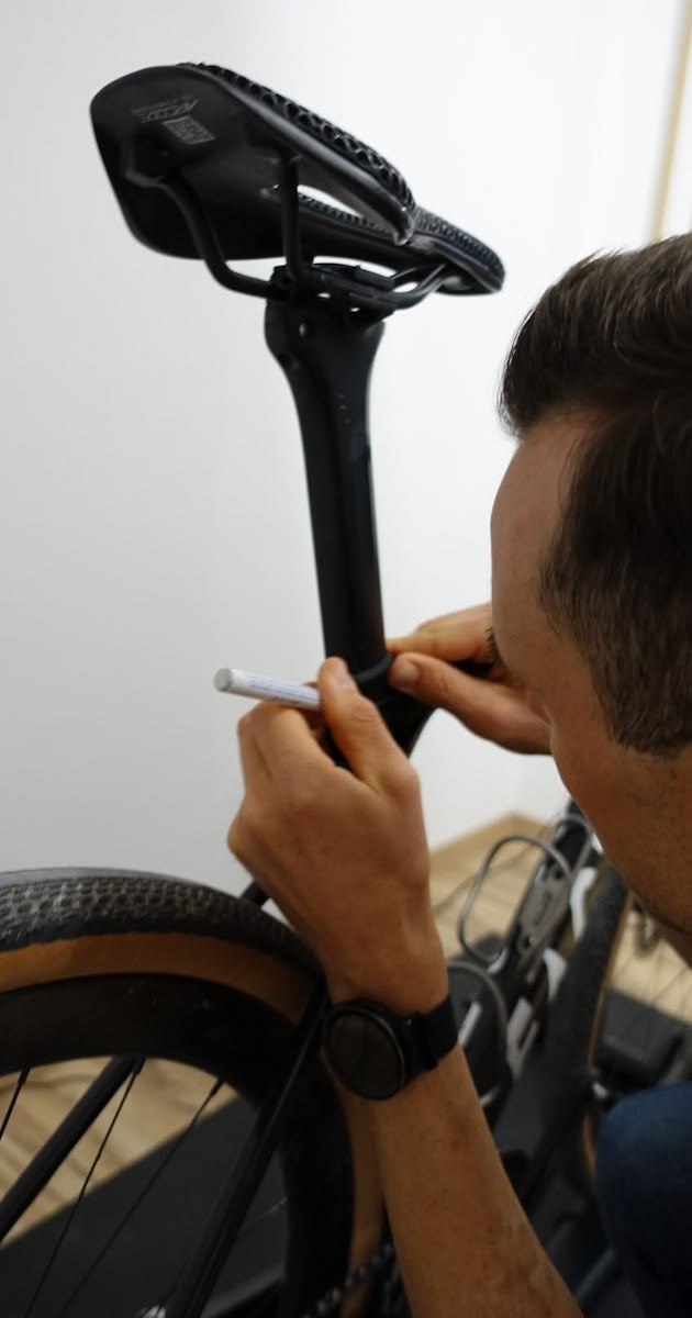 Person markiert die Höhe des Fahrradsattels mit einem weißen Stift an einem schwarzen Rennrad.