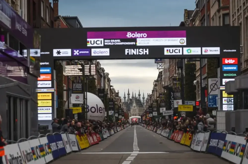 Ziellinie bei den UCI Gravel World Championships 2023 auf einer Straße mit Zuschauern und historischen Gebäuden im Hintergrund.