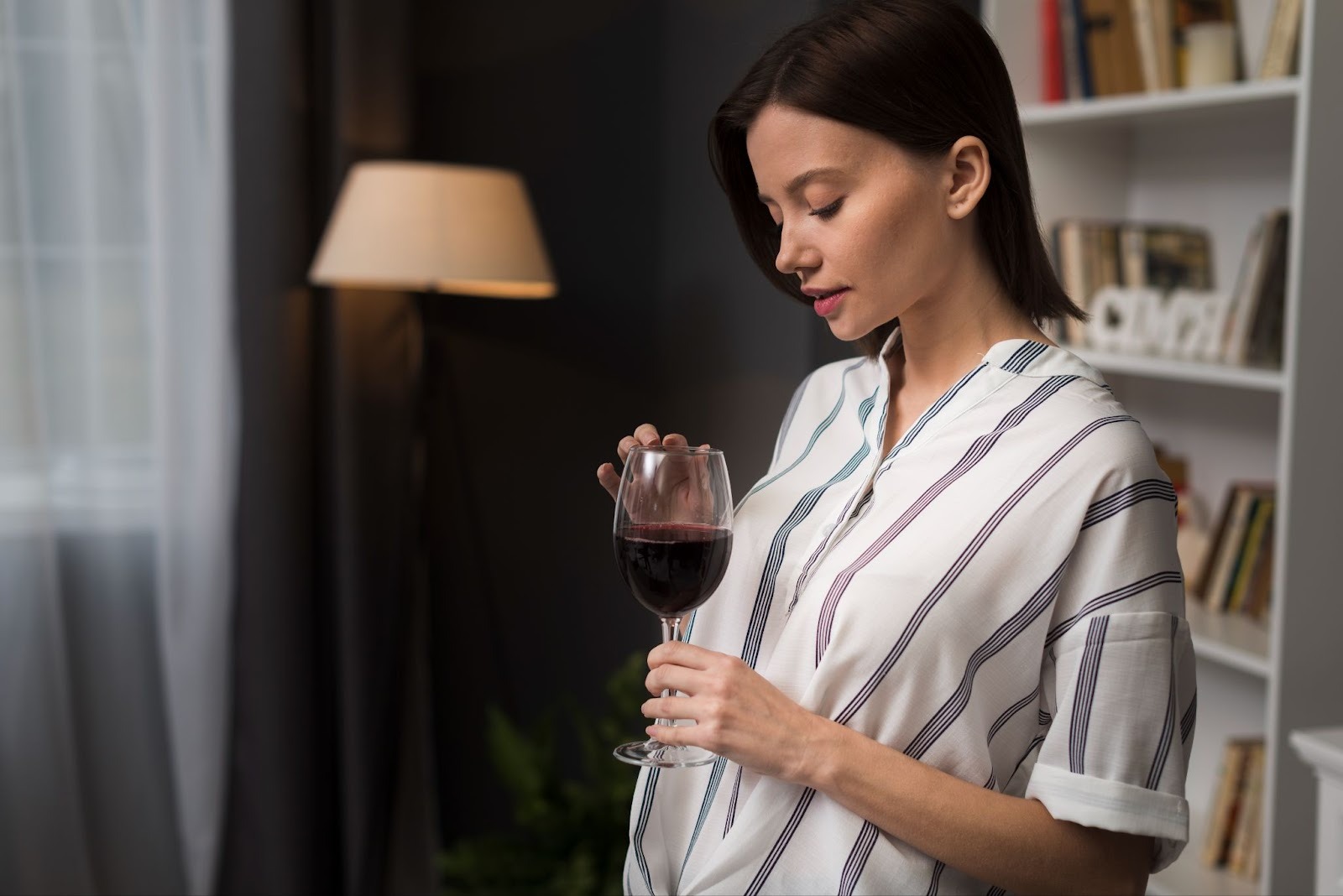 A calm seeming woman is looking in the red wine glass in one hand and touching the rim of that glass with another