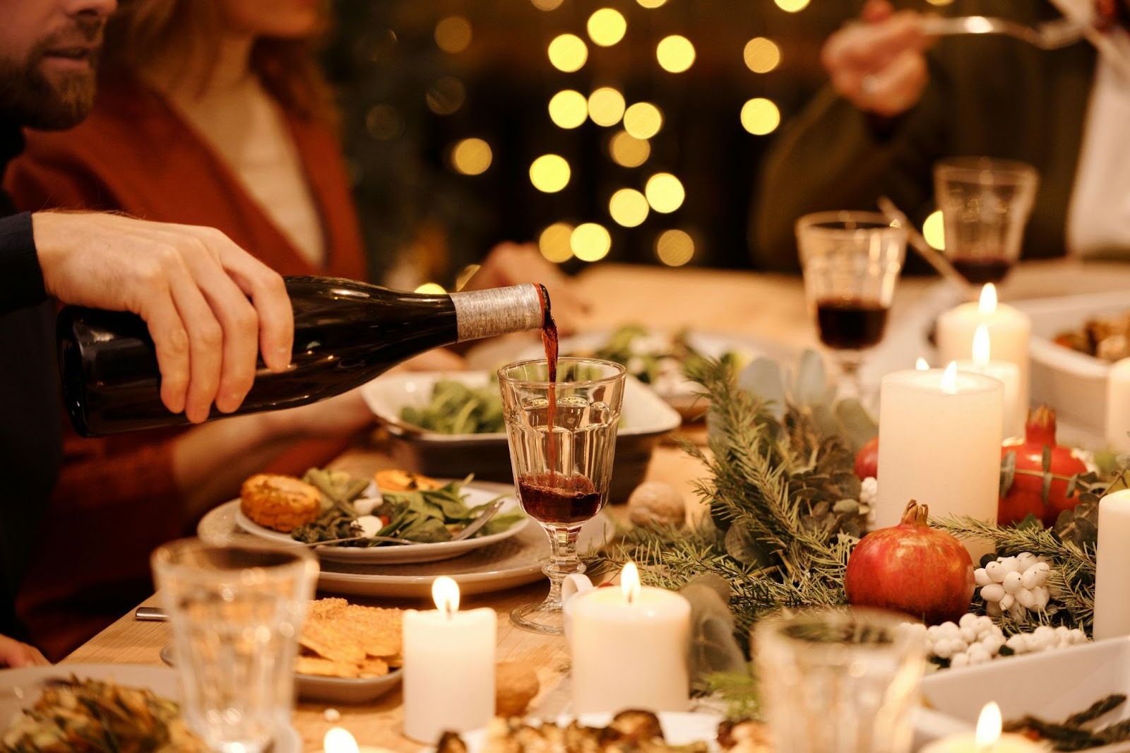 people sitting on a feasting table full of food and decorations a man is pouring wine in his glass