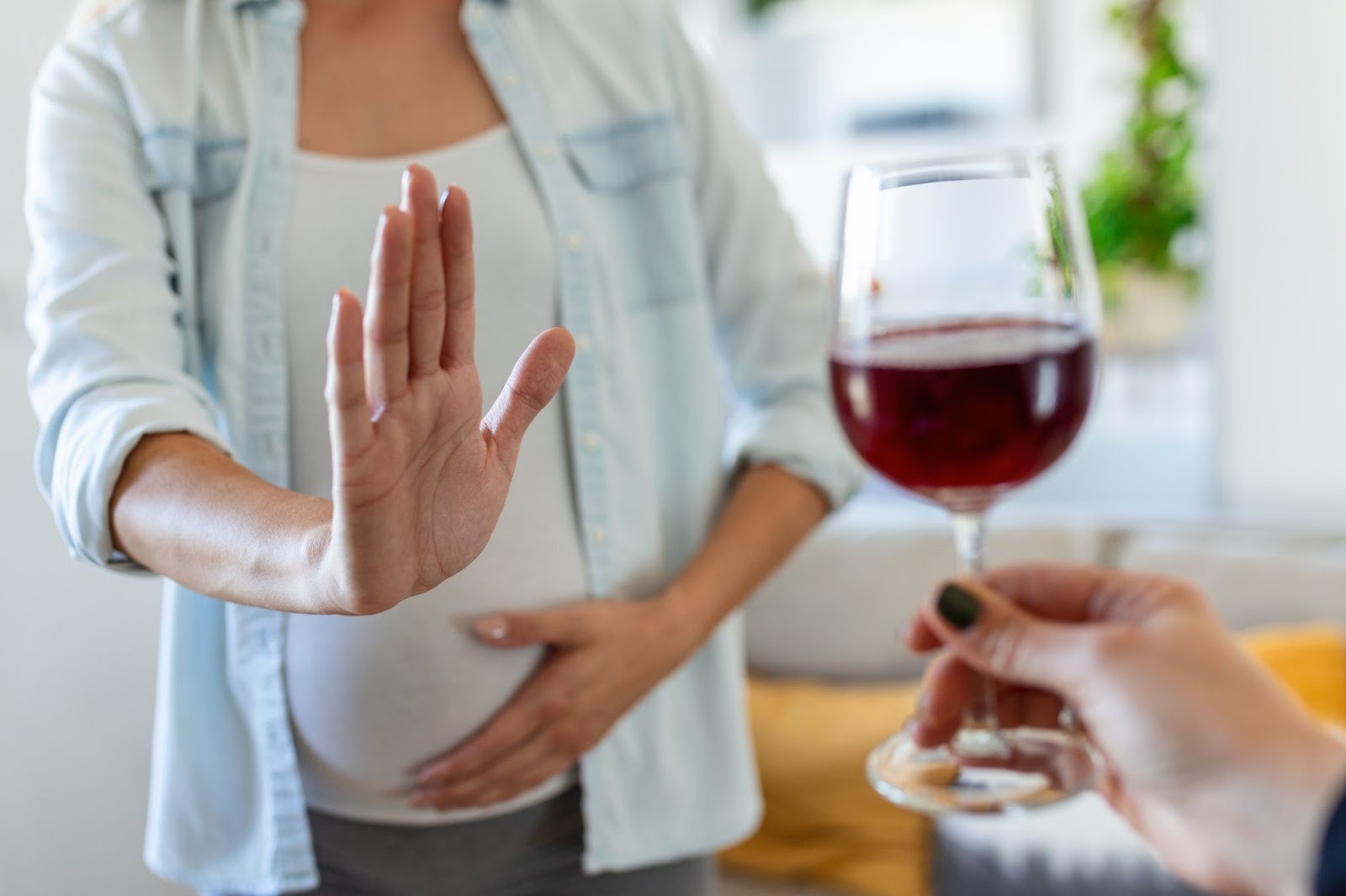 A pregnant woman showing a stop hand gesture to a wine glass offered to her.