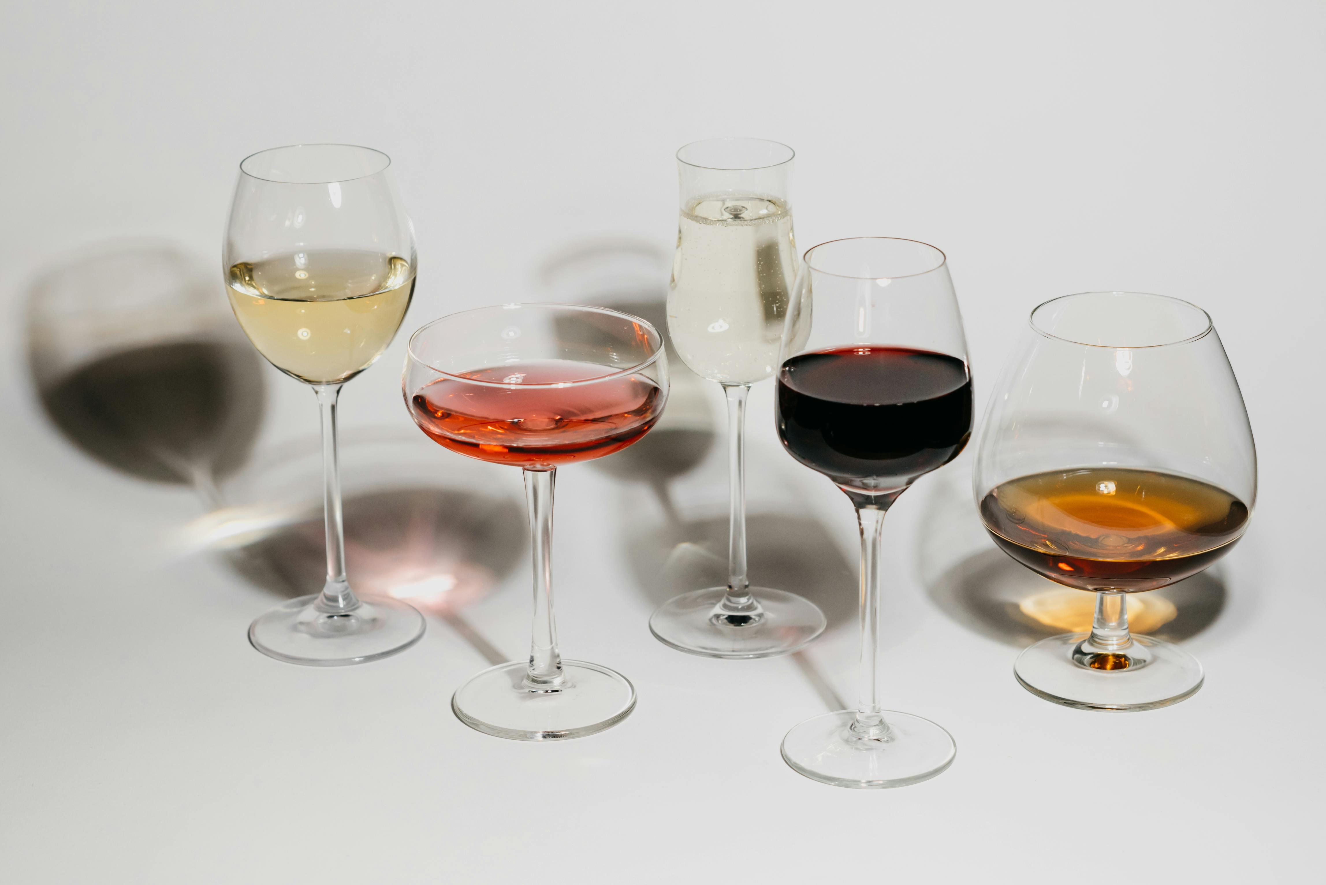 Five different types of wine glasses with different wines are placed on a white surface
