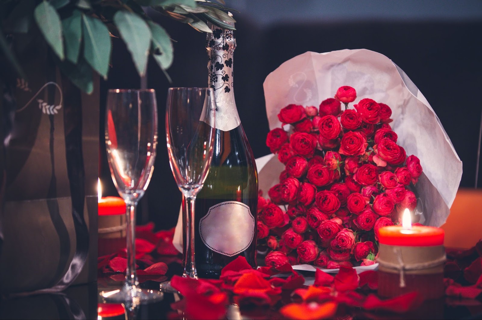 A red rose bouquet, a wine bottle two glasses and candles on a platform