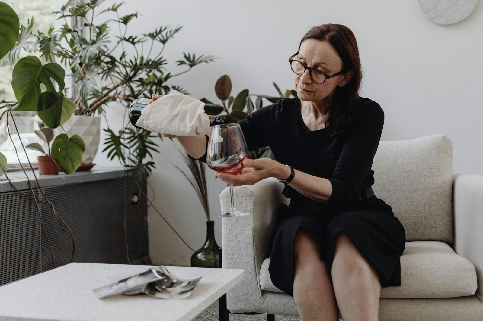 A woman sitting on couch pouring wine into her glass