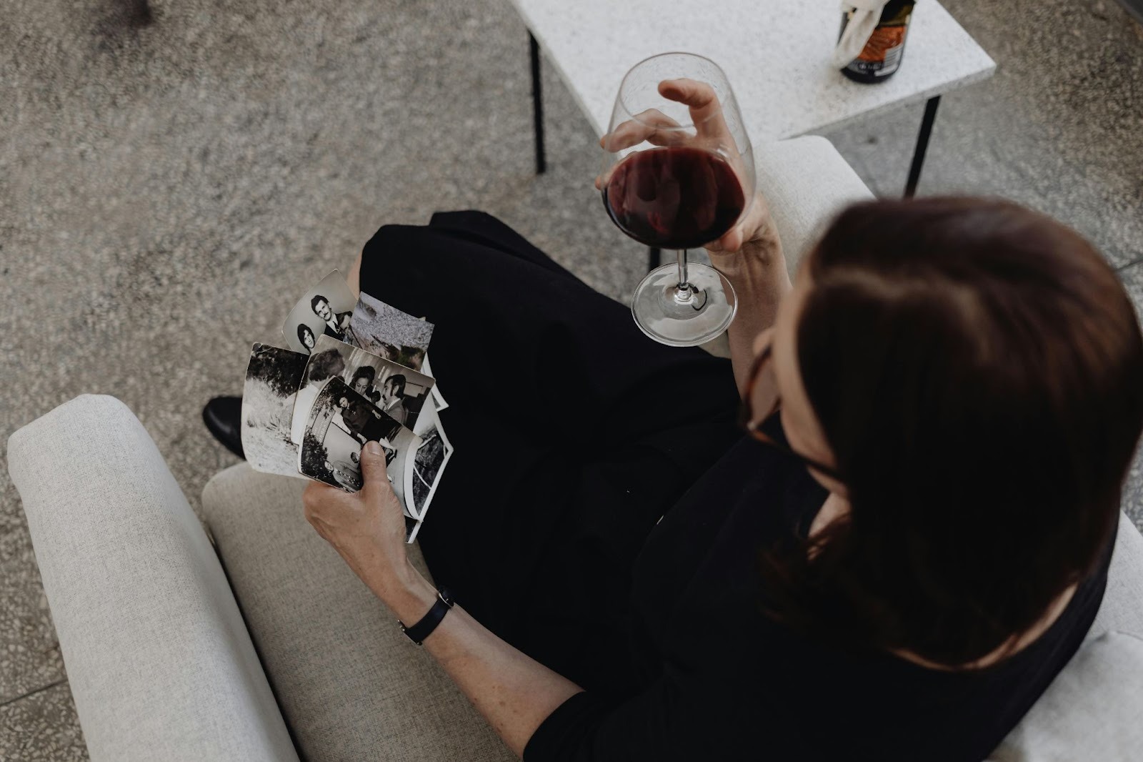 A woman sitting on couch with a wine glass in right hand and some old photographs in left